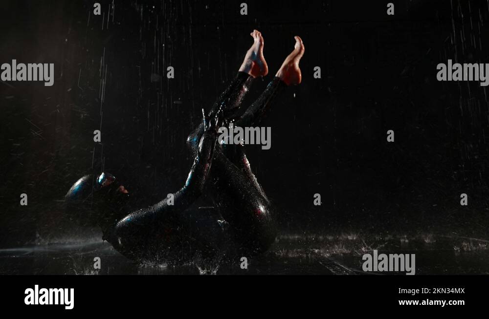 unrecognized woman in black latex suit and mask is lying in puddle in ...