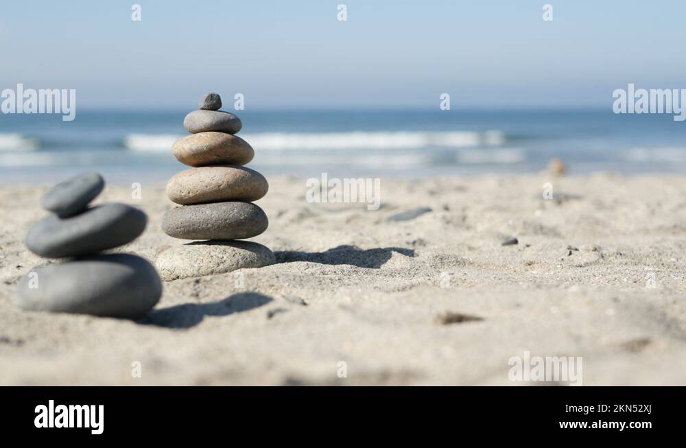 Rock balancing on ocean beach, stones stacking by sea water waves ...