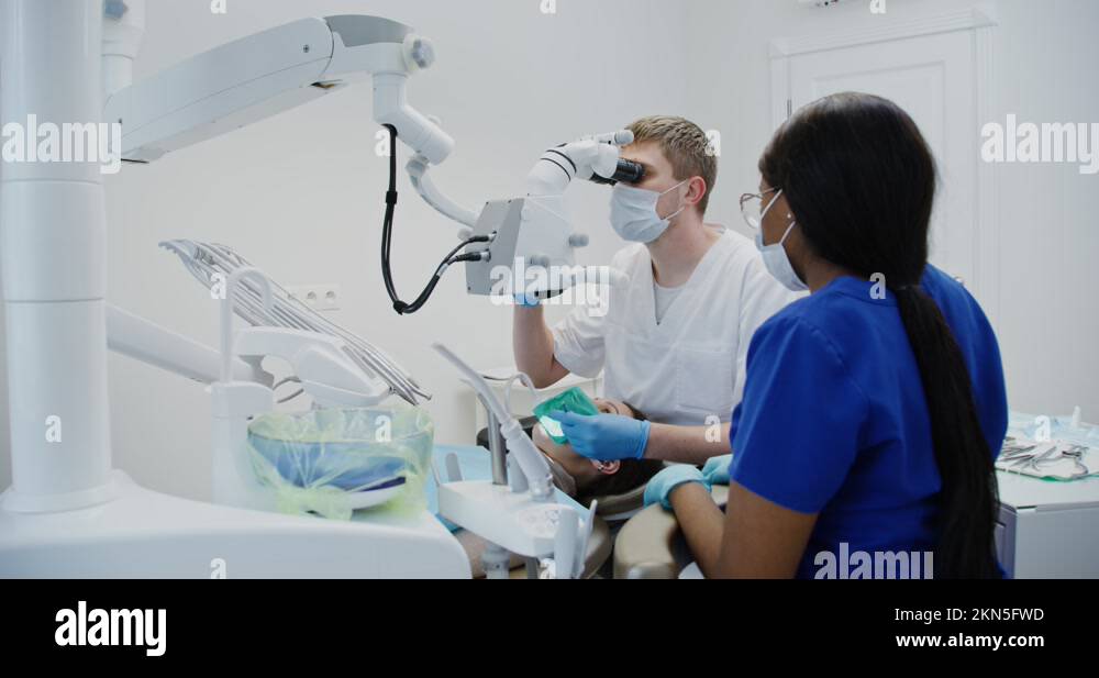 Male dentist looks through dental microscope for patient's tooth root