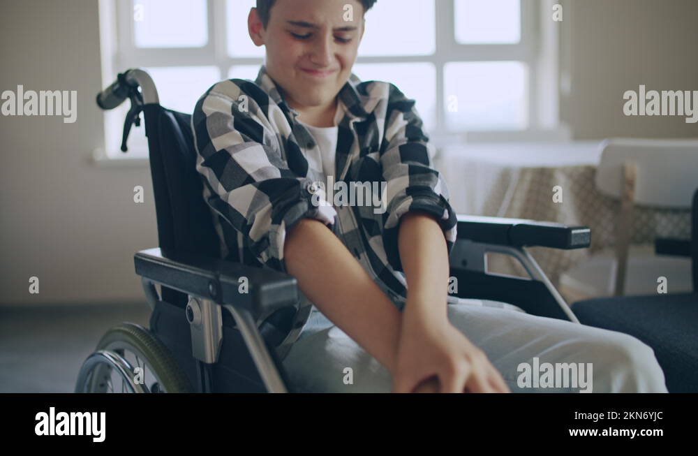 Teenager in wheelchair massaging knees, rehabilitation after injury