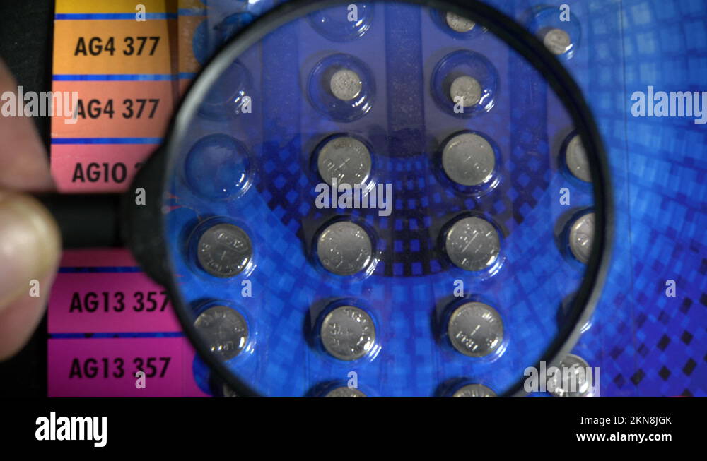 Hand using a magnifier / magnifying glass to see codes on button batteries Stock Video Footage