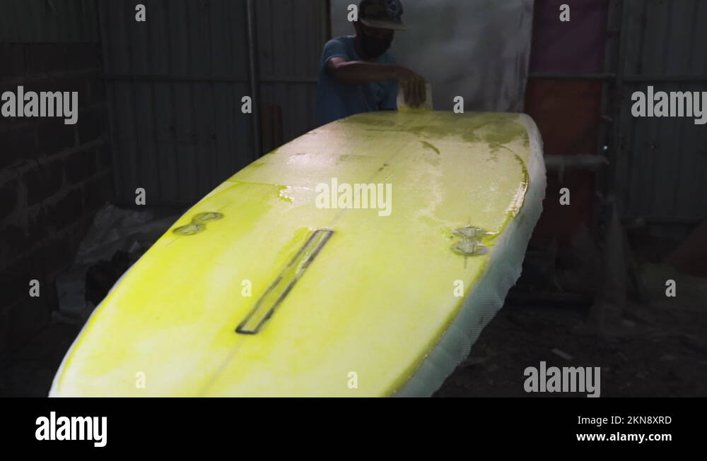 Worker applying epoxy resin on foam during making of new surfboard at