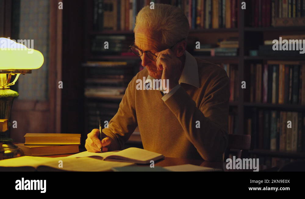 Senior male writer working on a new book, taking notes in library late ...