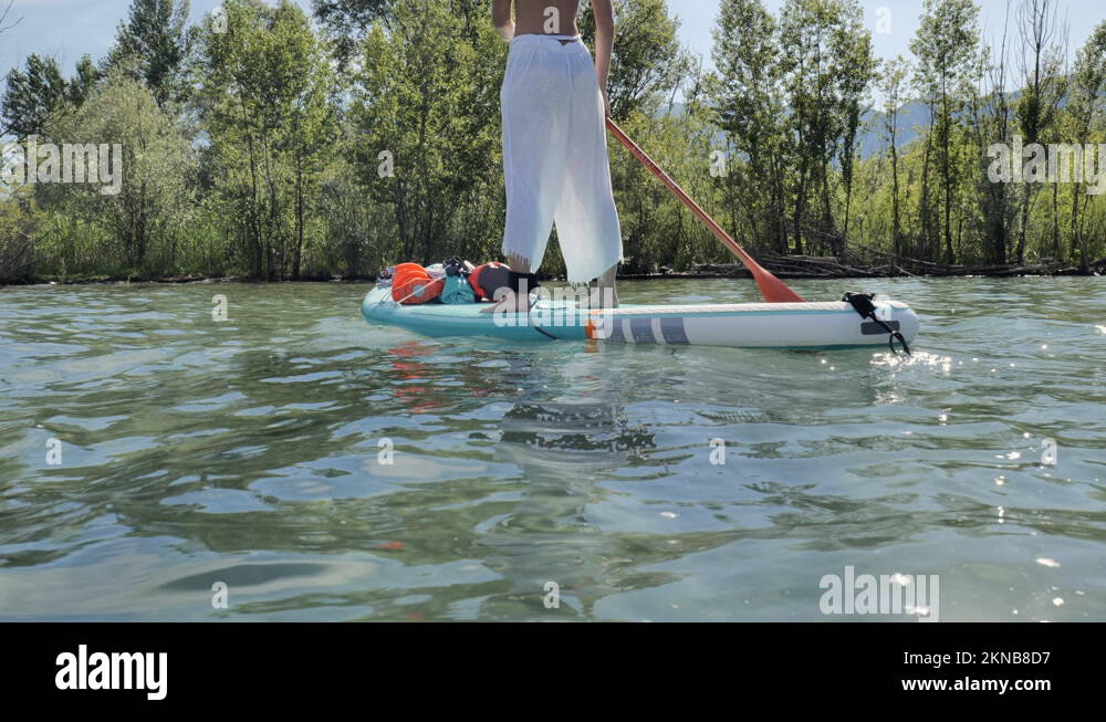 Young sportive woman on a stand up paddle board rowing on calm lake