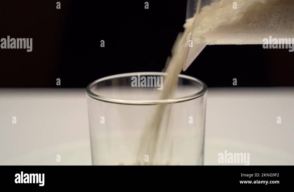 White rice is poured from a measuring cup into a transparent container ...