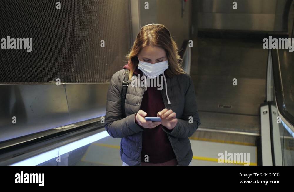 Student on escalator wearing facial mask uses mobile phone in the metro ...