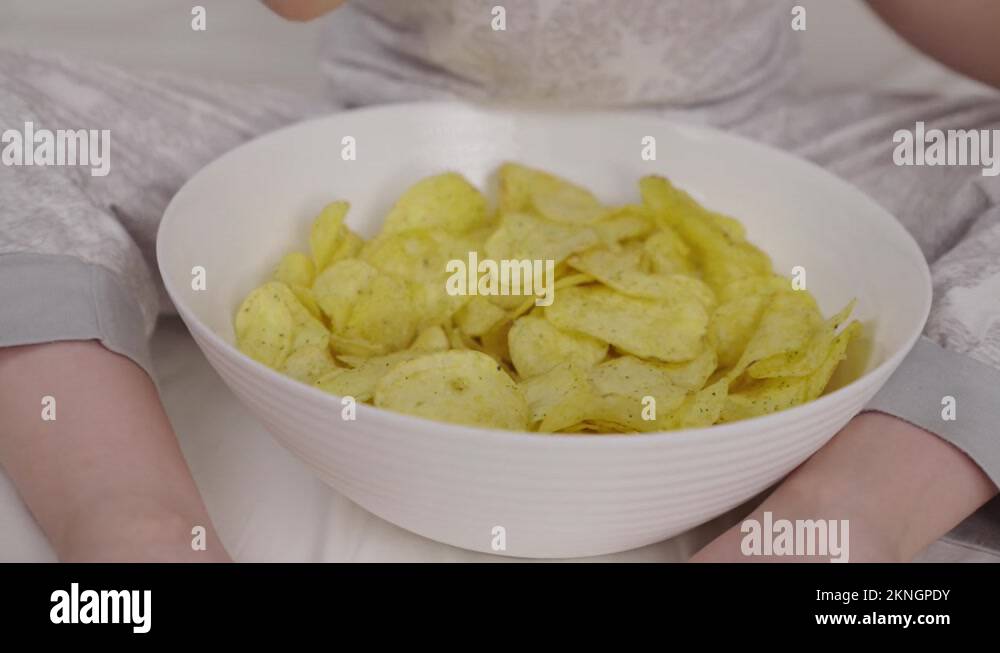 Little child eats potato chips from plate lying on bed in the bedroom, delicious Stock Video