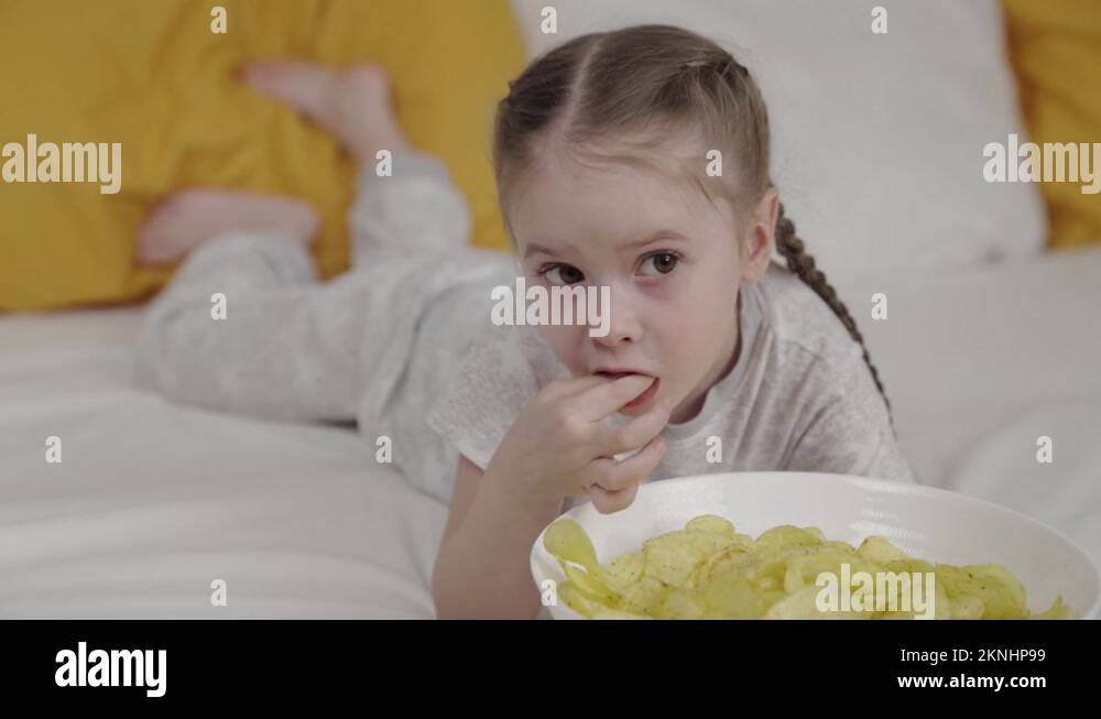 little child eating potato chips lying on bed in bedroom, delicious crispy fatty Stock Video