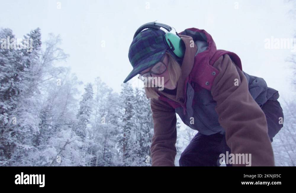 HANDHELD ACTION woman uses a chainsaw to cut ice bathing hole Stock