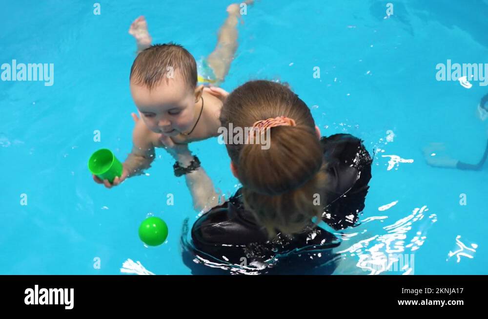 Newborn baby in swimming pool with coach. Instructor teach child to