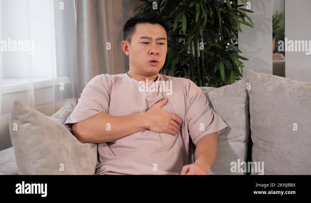 Sick heart Trouble breathing, chest pain, Asian man sitting on couch at