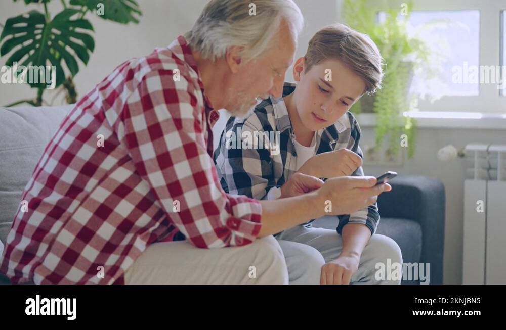 Teen boy teaching grandfather how to use smartphone, family support and
