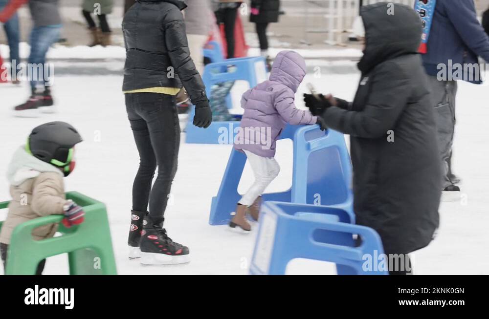 Young child skates on ice skating rink with trainer object, wearing