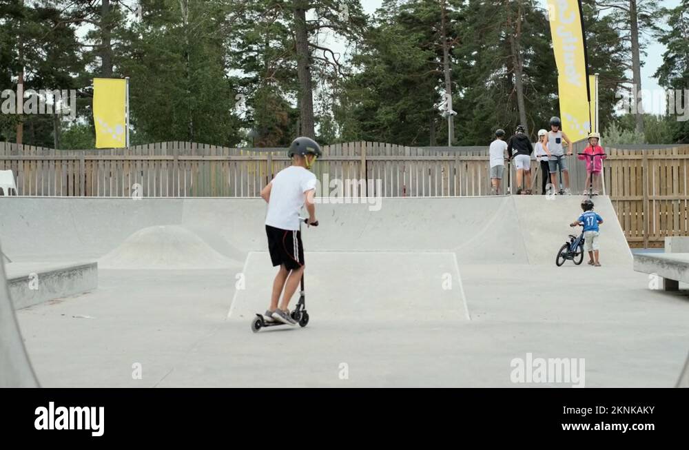 Young blonde lad boy jumping scooter kick bike of ramp concrete skate ...