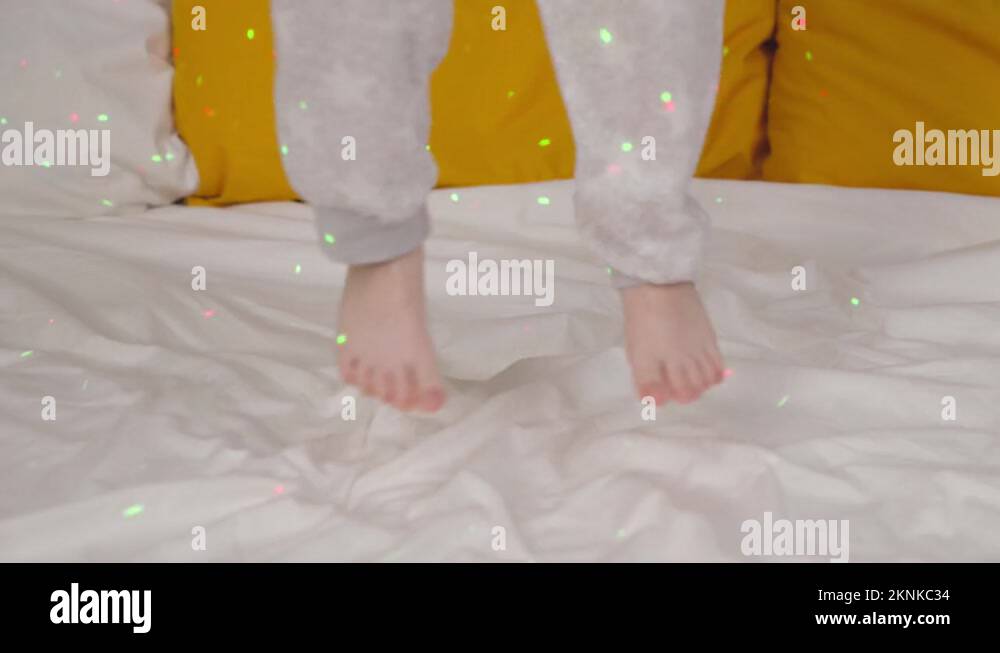 little child jumping on the bed in bright colors of light, baby feet