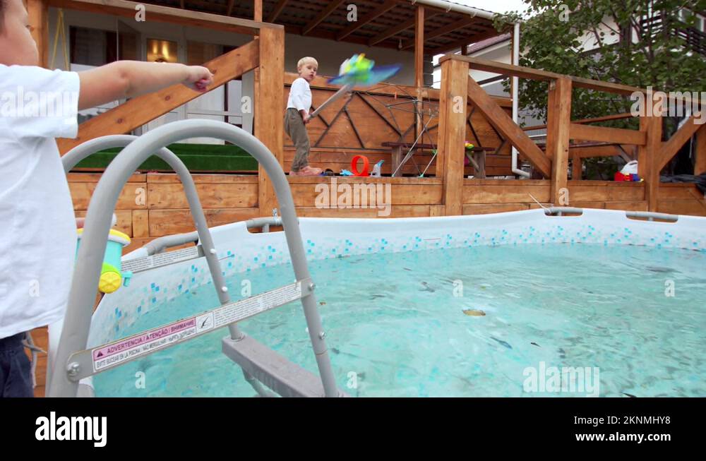 Boys trow and catch toys from the swimming pool using pool cleaning net on pole Stock Video