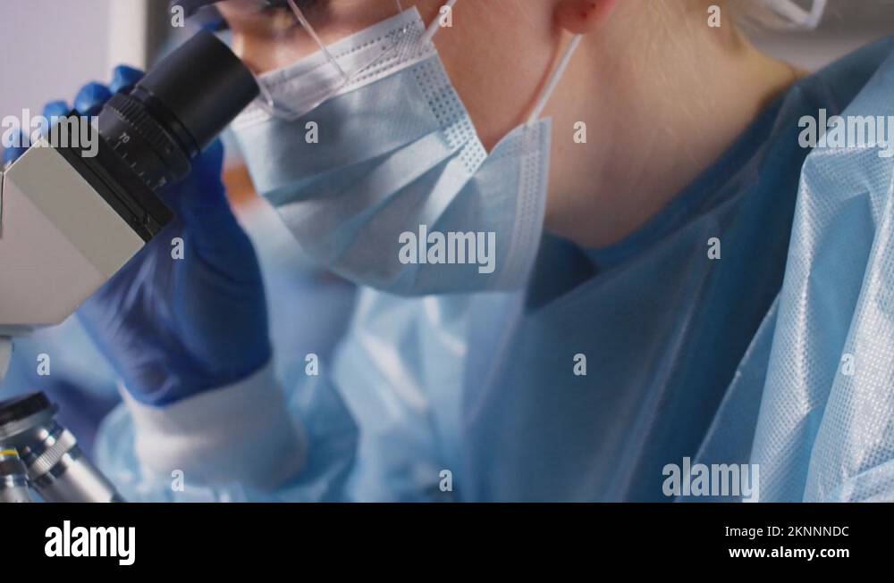 Female Lab Worker Wearing PPE Analysing Samples With Microscope Holding ...