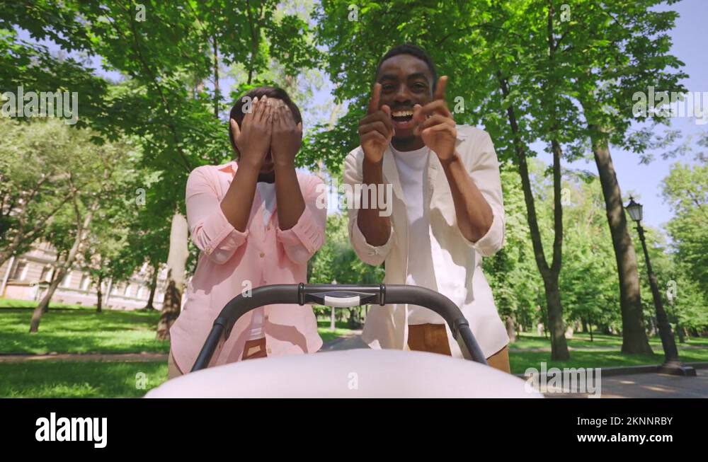 Funny black parents playing peek-a-boo with baby in stroller, making child laugh Stock Video 
