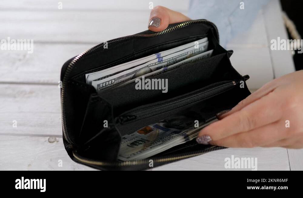 A closeup of a woman opens a purse full of hundreddollar bills Stock