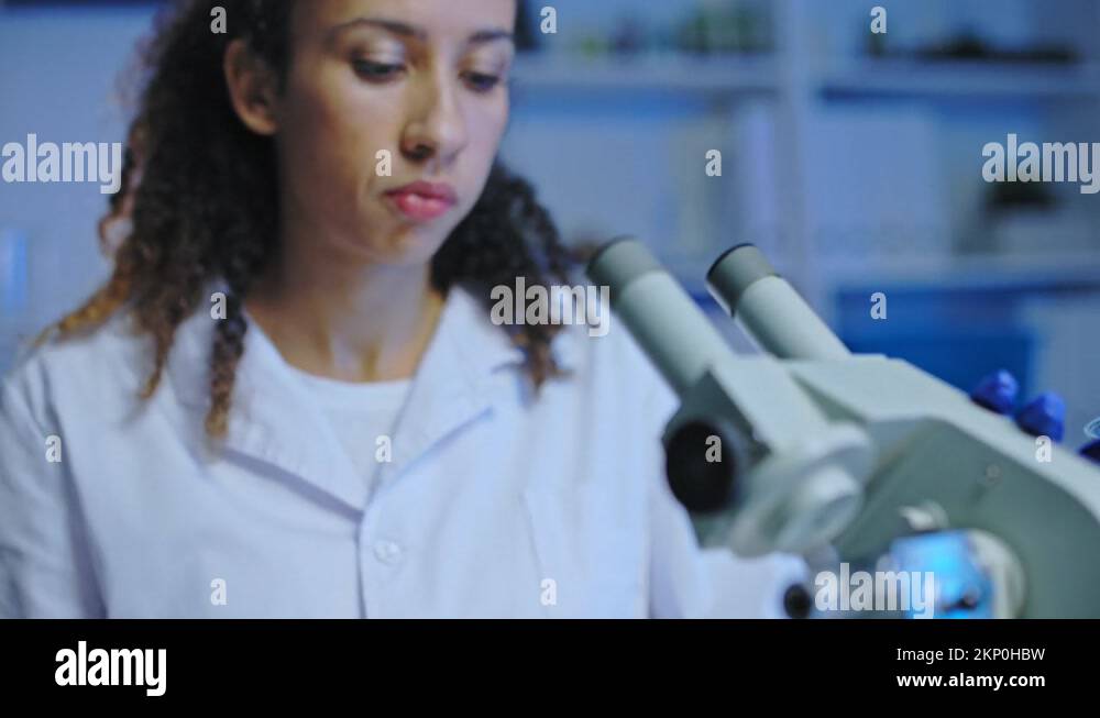 Female lab assistant examining sample under microscope, testing product ...