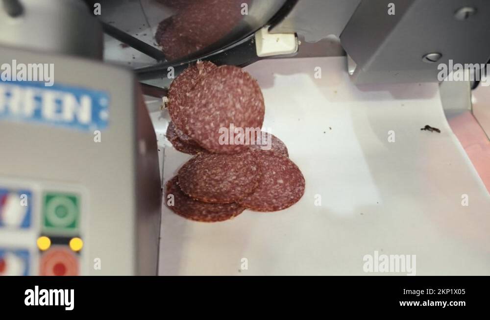 Salami slices dropping from a commercial meat slicing machine at a