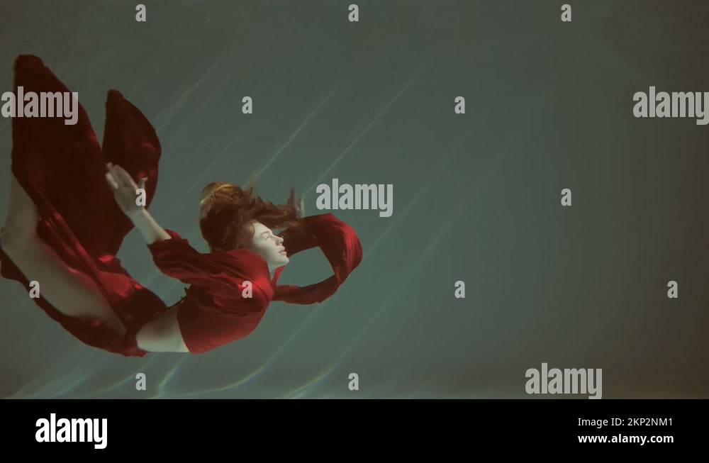 Attractive red-haired young woman swims beautifully underwater in a red