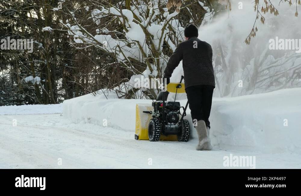 Man using snow plow machine to clear the driveway to the road in winter