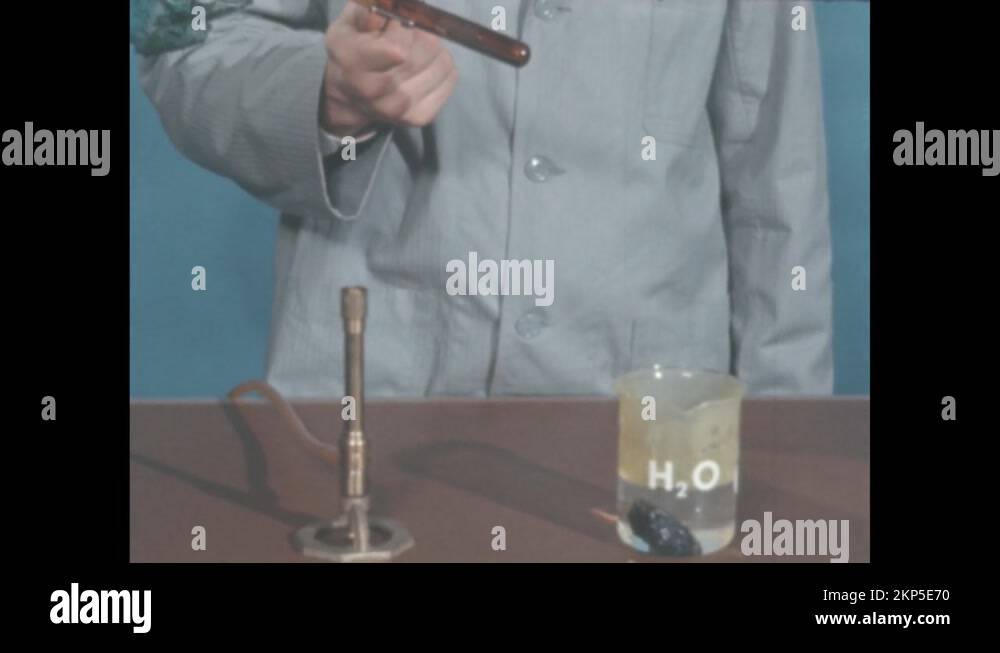 1960s Person holds test tube. Bunsen burner and beaker full of water