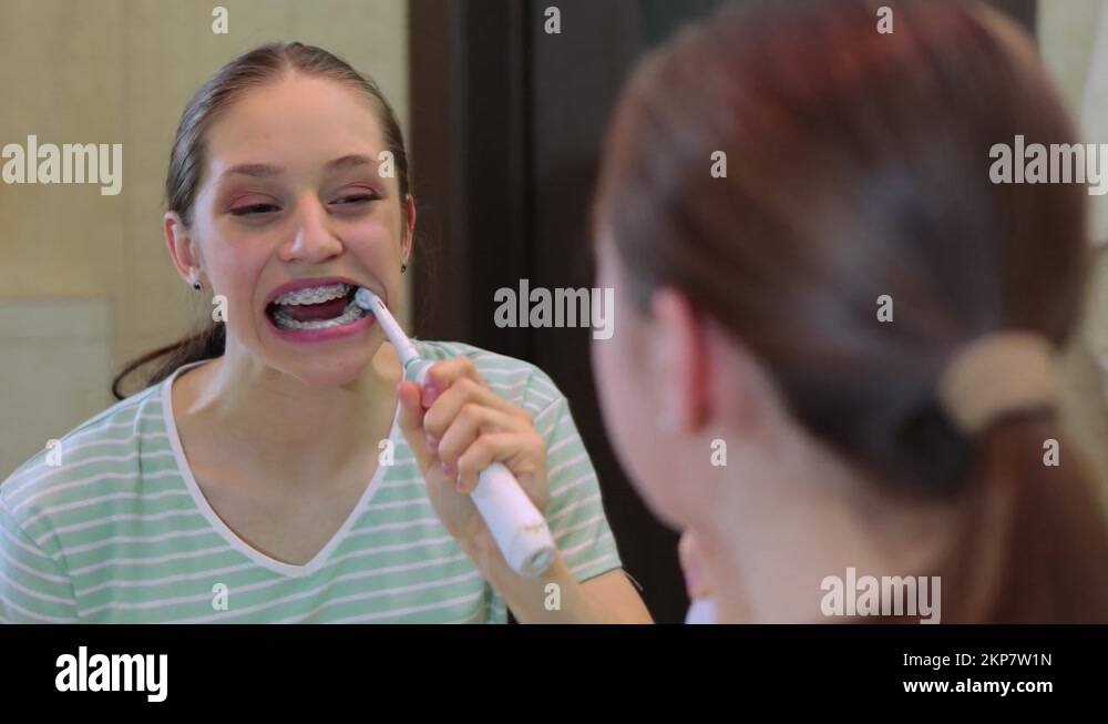Young female brushing teeth with braces in the bathroom. Health care