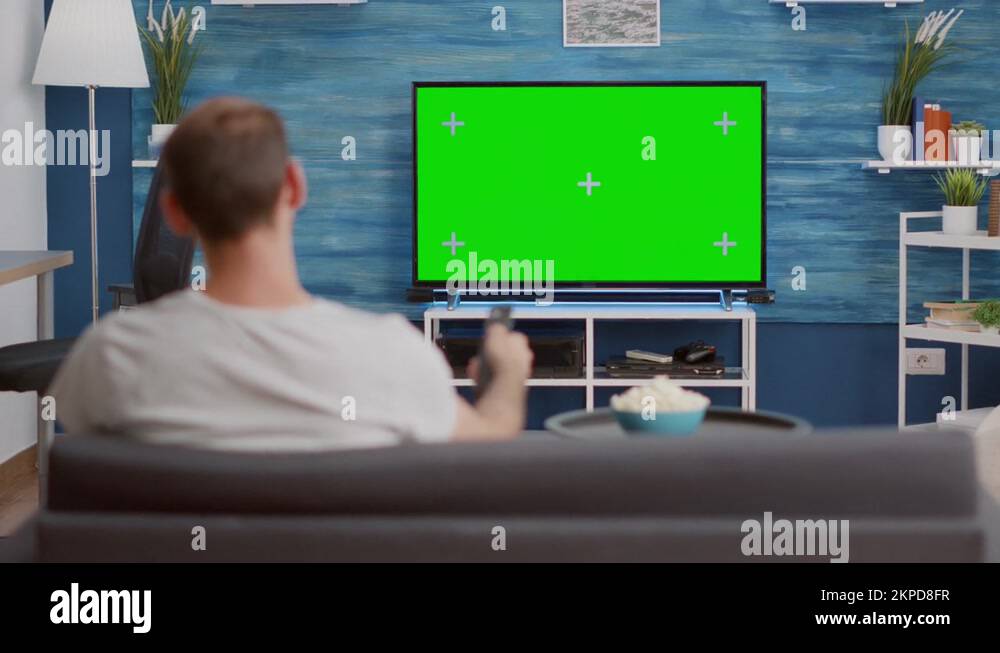 Man looking at green screen on tv and switching channels sitting on