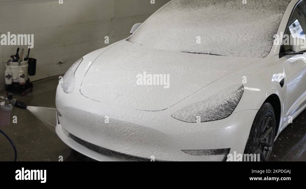 Tesla Model 3 getting carwash with foam cannon on the front end Stock