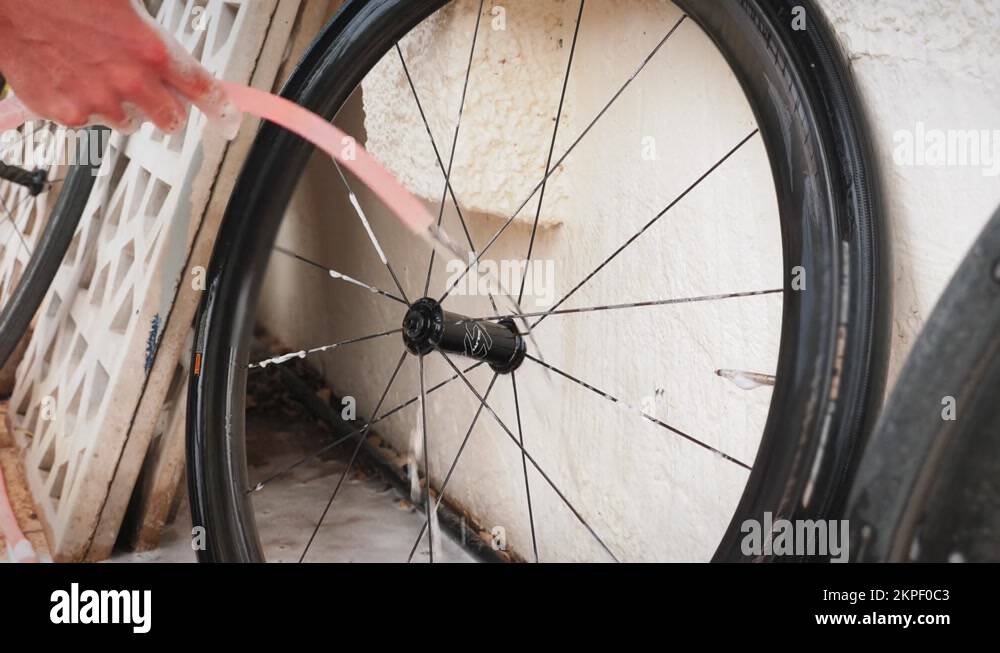 Man washing road bike wheel with water from hose. Bike mechanic