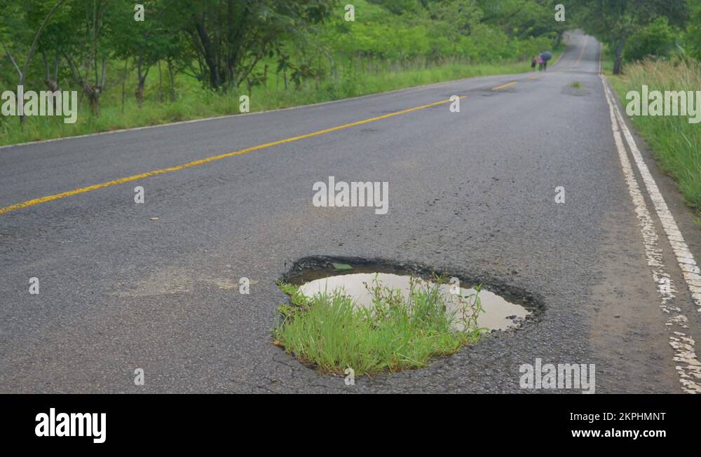 LOW ANGLE Grass grows around a gaping hole in the road filled with