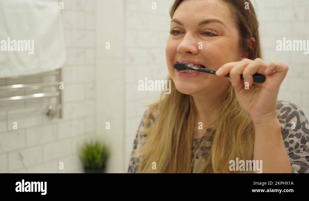 woman with long blond hair brushing her teeth with toothpaste in front