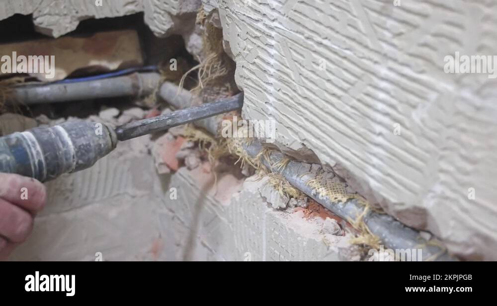 Plumber using a jackhammer to drill into wall, replaces old water pipes
