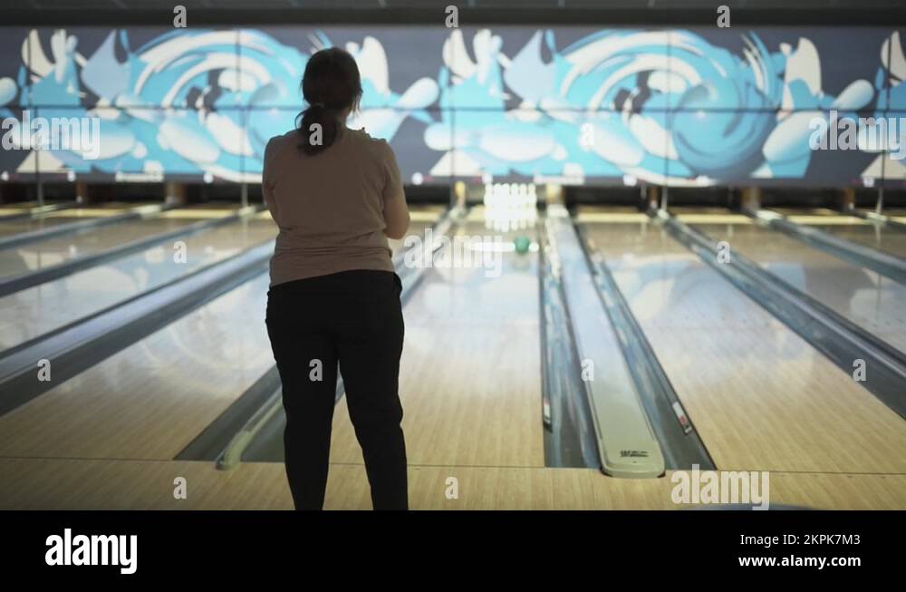 Woman runs up in approach zone and throws green ball into a bowling alley Stock Video Footage