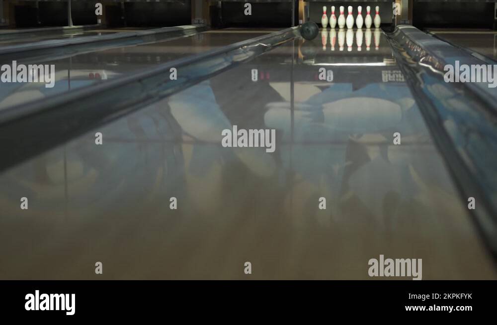 Dark green ball rolls down shiny smooth wooden lane in bowling alley