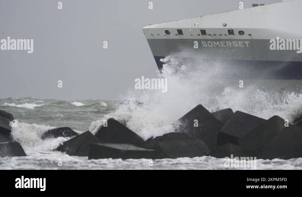 Slo motion shot of ship sailing out a port, as waves crash over jetty