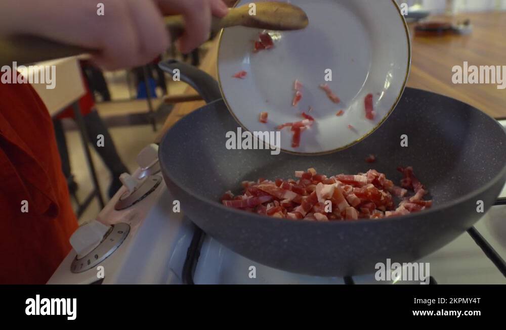 Chef cook frying and stirring chopped bacon lardons meat in large pan