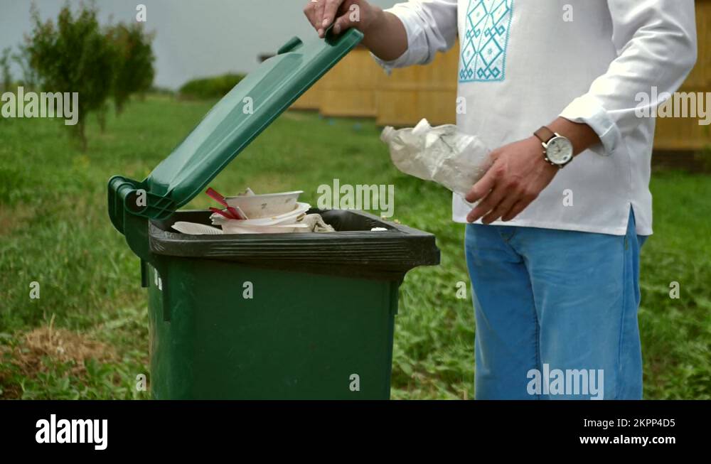 A faceless white man throws recyclable plastic bottles into a trash can