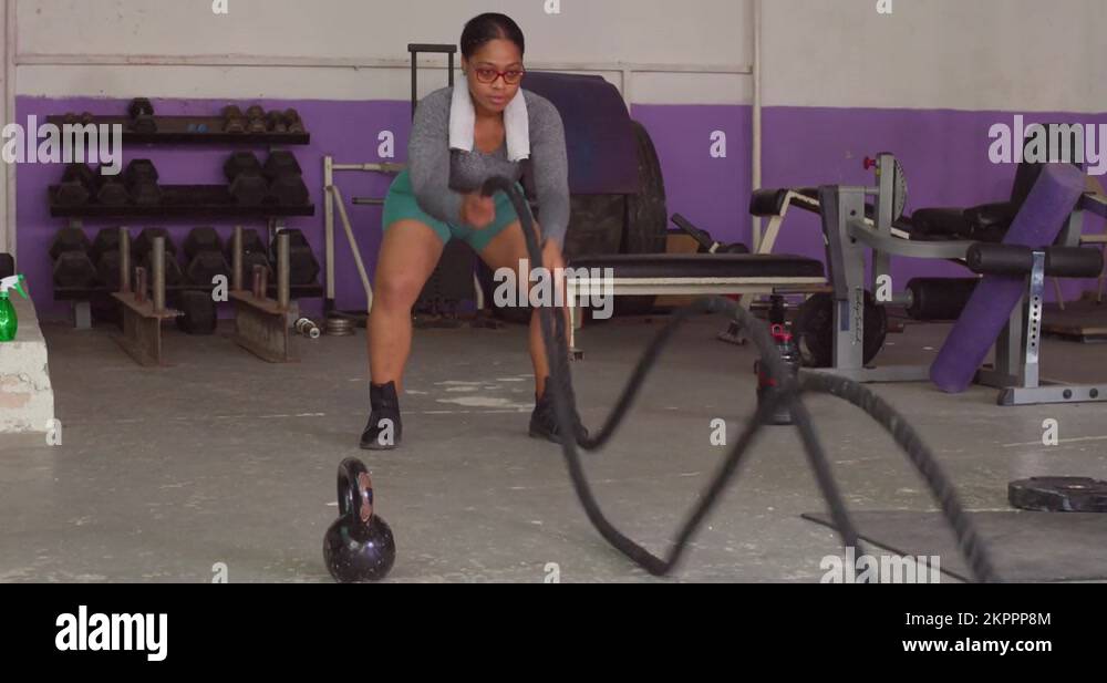 Young fitness model using battle ropes at the gym in sports wear low ...