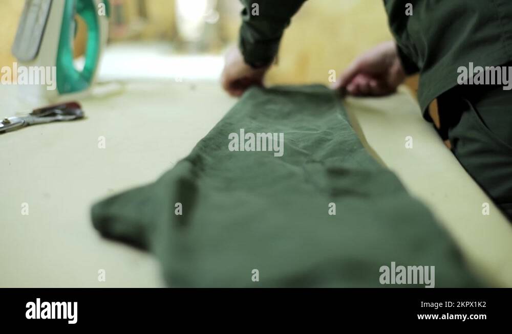 swede aligns the green pants of a military uniform on an ironing board