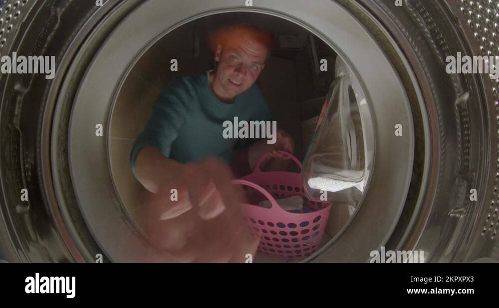 A male cleaner throws dirty laundry into the washing machine Stock