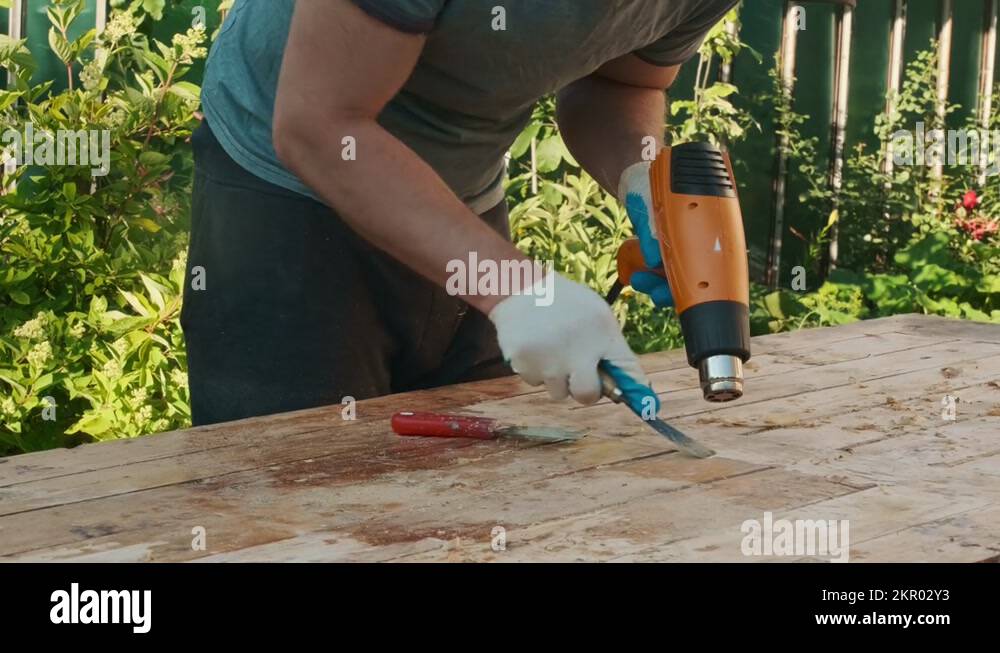 Man removing old varnish from wood using scraper and heat gun Stock