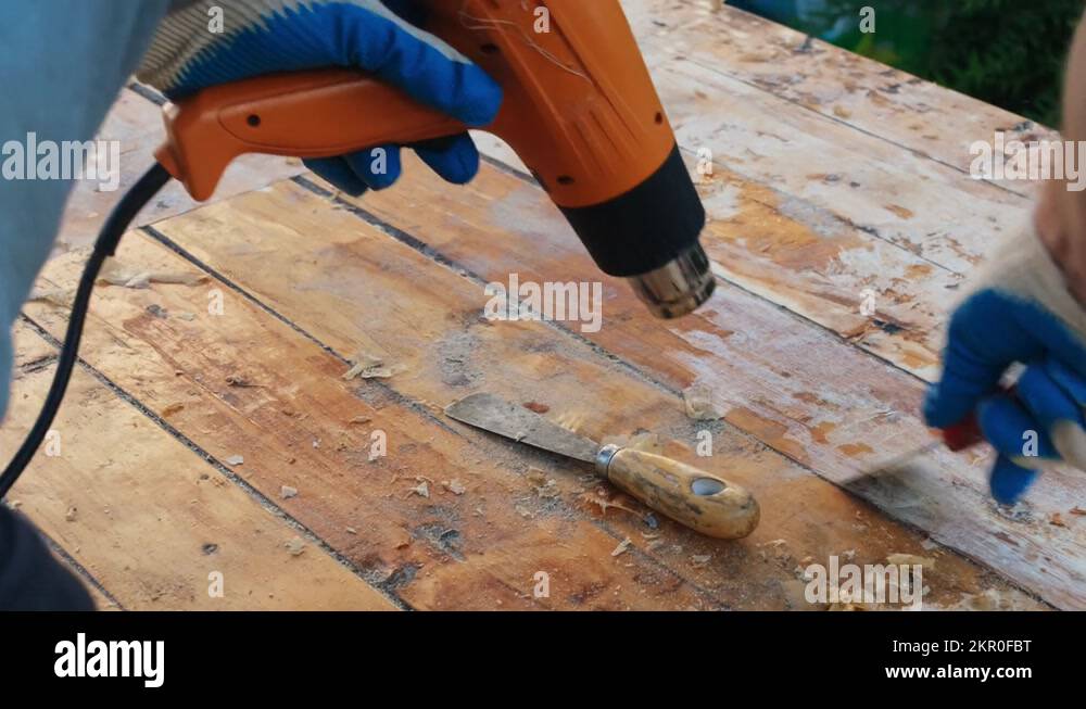 Man removing old varnish from wood using scraper and heat gun Stock