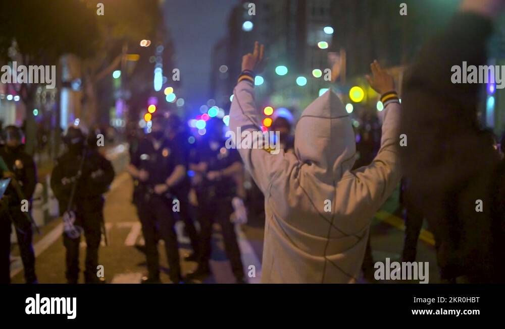 A Black Man in a hoodie holds up his hands in front of a line of riot ...