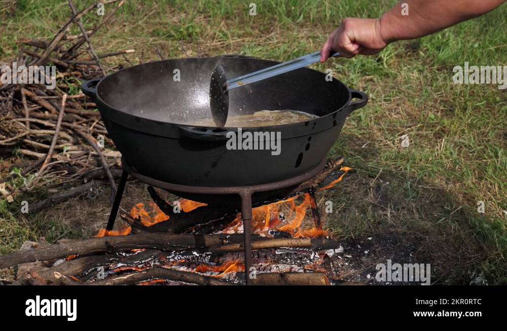 cooking KULESH. mixing millet porridge in a castiron cauldron on fire