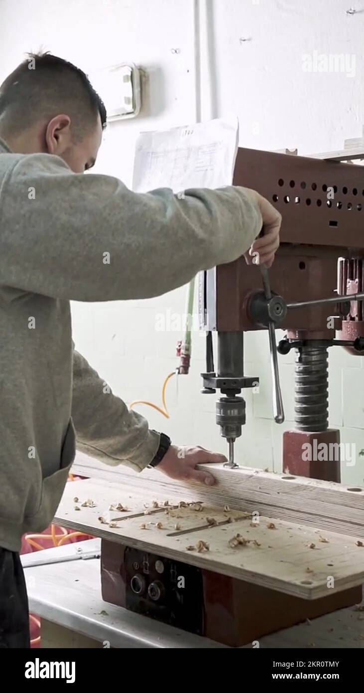 Man drills holes in wooden planks with bench drill machine. Furniture