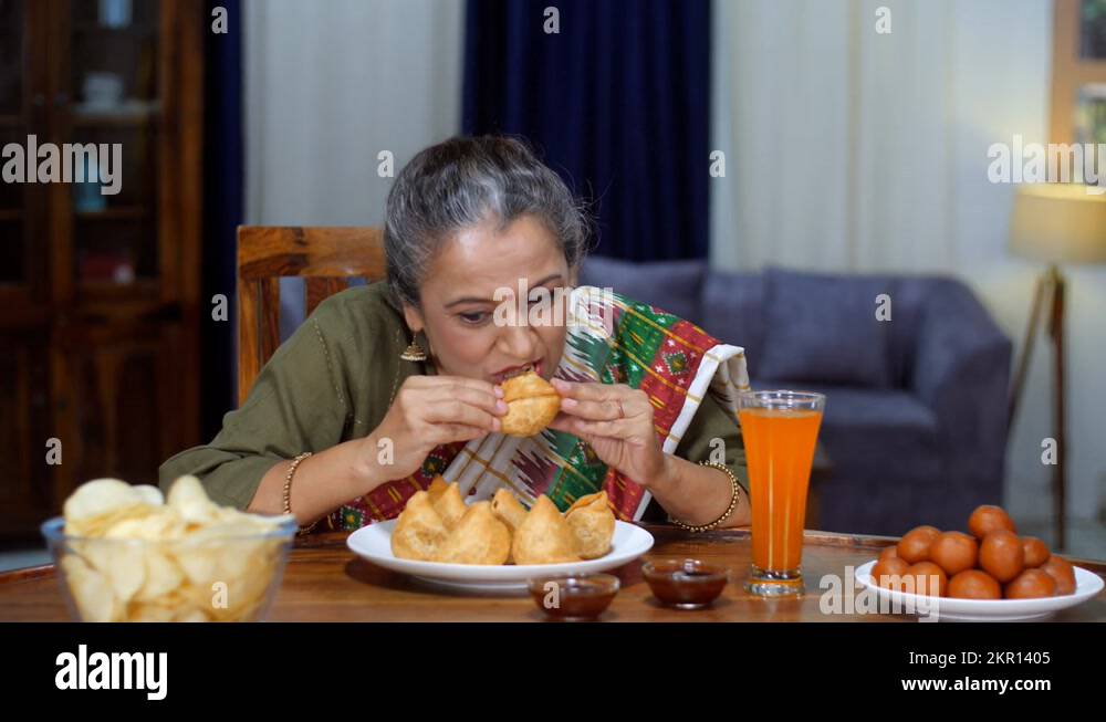 An aged Indian housewife eating Samosa - Indian street food, deep-fried ...