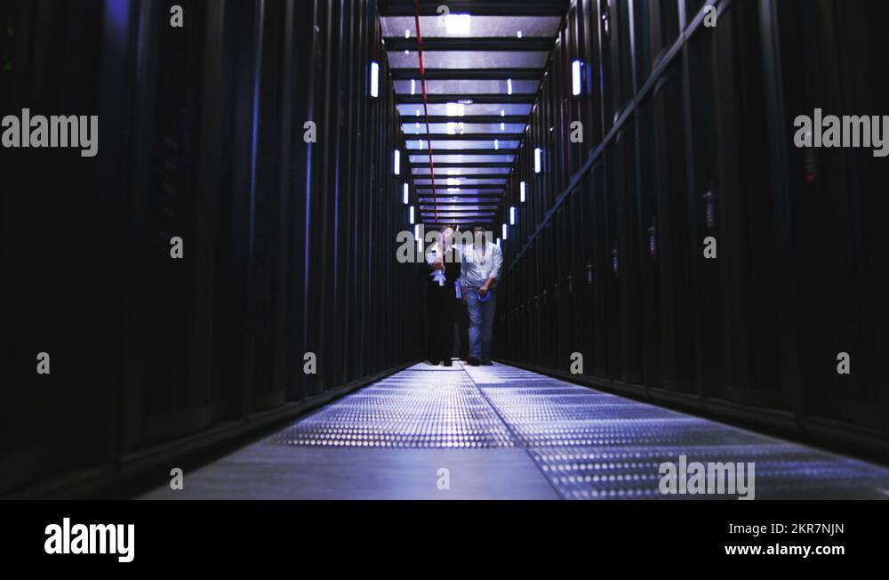 People working in computer server room data center. Walking along rows ...